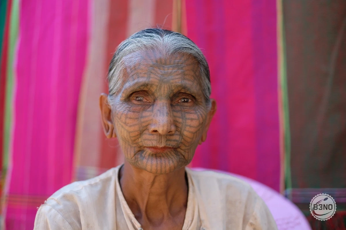 Femme chin au visage tatoué devant un tissu rose, région de Mrauk-U — Mrauk U, Voyages